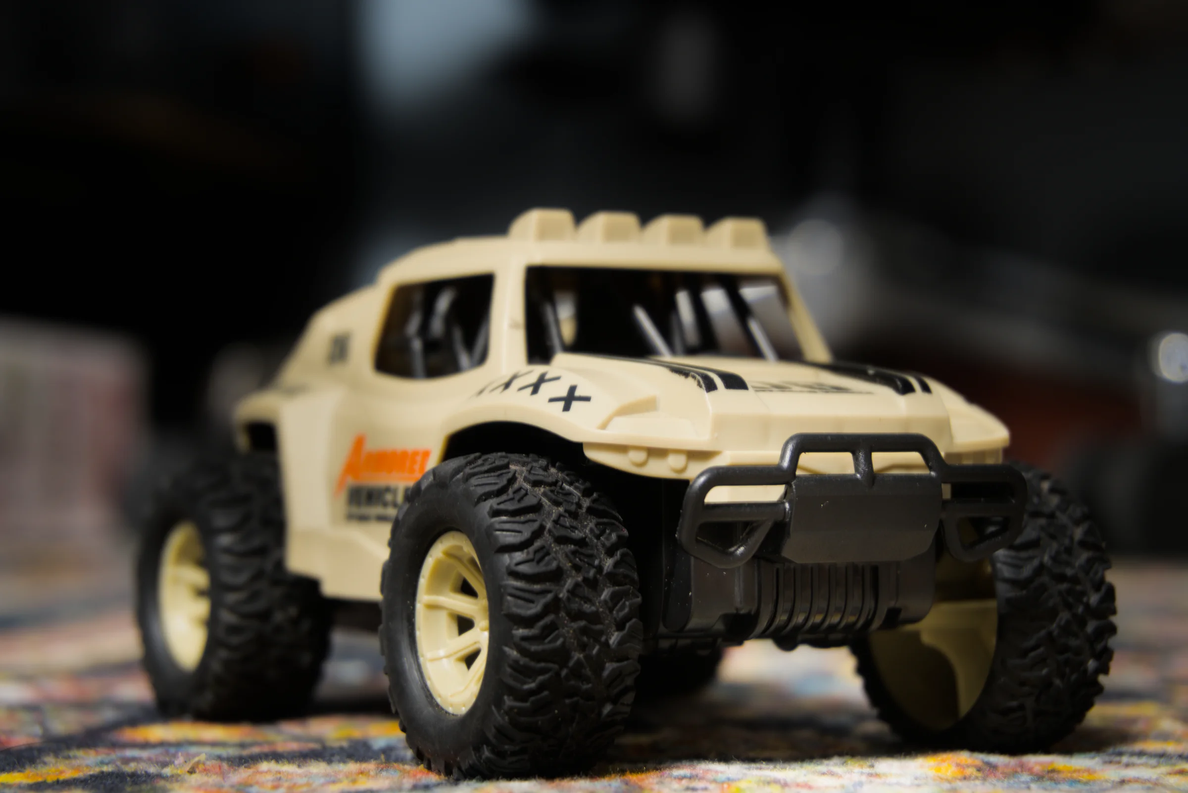 A yellow and black toy off-road truck photographed close up on a patterned mat, the background thrown completely out of focus.